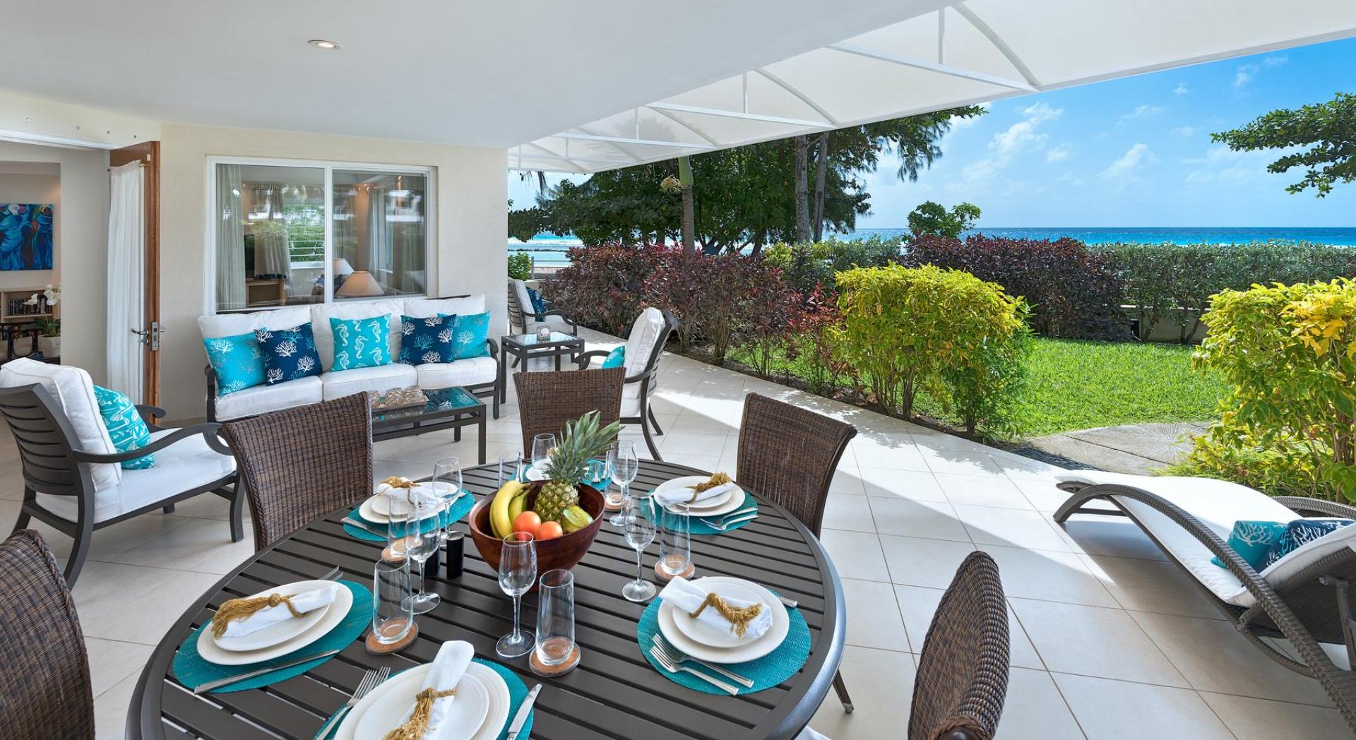 A spacious covered patio at Palm Beach 101 in Barbados, featuring an outdoor dining table, lounge seating, and breathtaking ocean views.