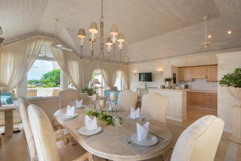 Beautifully appointed dining area at Forest Hills 23, Barbados, featuring a grand chandelier, a six-seater table, and an open-plan kitchen.
