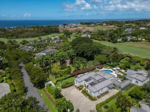 Aerial view of Ixora at Royal Westmoreland, showcasing the lush greenery, pool, and surrounding villas with a glimpse of the ocean