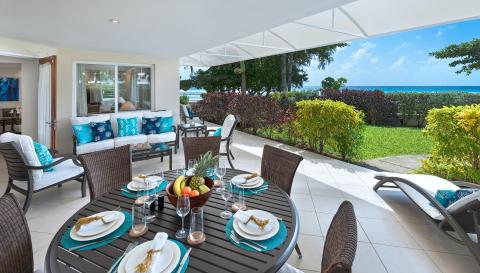 A spacious covered patio at Palm Beach 101 in Barbados, featuring an outdoor dining table, lounge seating, and breathtaking ocean views.