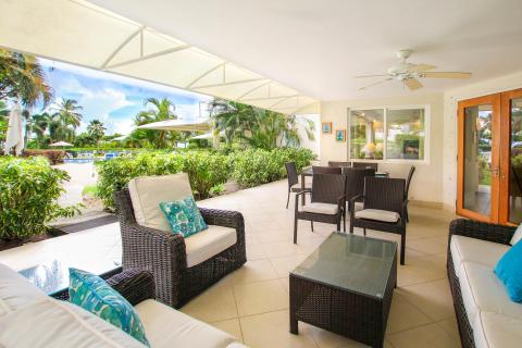 Spacious covered patio at Palm Beach 109, Barbados, featuring plush seating, tropical garden views, and access to the resort-style swimming pool.