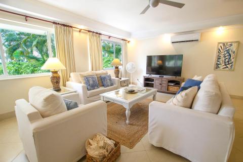Cozy entertainment area at Palm Beach 109, Barbados, with a large flat-screen TV, plush seating, and tropical garden views.