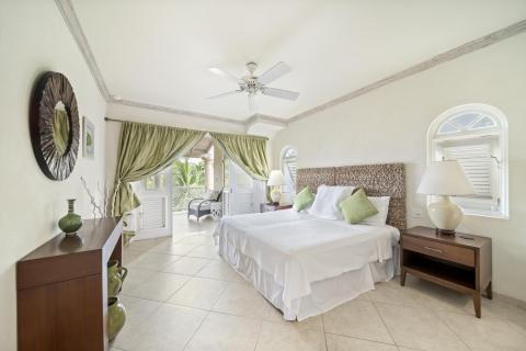 Elegant bedroom in Sunshine View Penthouse, Sugar Hill Resort, Barbados, with a comfortable queen-size bed, soft green accents, and direct access to a private balcony with views of tropical palm trees, creating a serene and restful atmosphere.