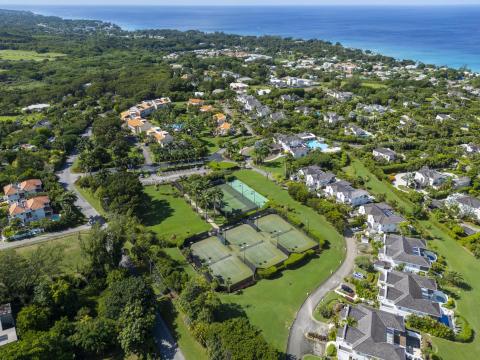 Expansive aerial view over Sugar Hill Resort and surrounding luxury estates in Barbados, with clear views of the resort’s central pool and tennis courts, and the stunning Caribbean Sea in the background.