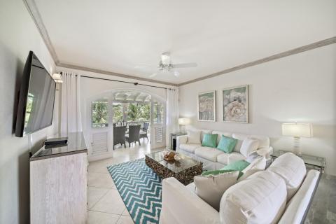 Bright and inviting living room in Sunshine View Penthouse, Sugar Hill Resort, Barbados, with elegant coastal decor, comfortable white sofas accented by turquoise cushions, and large glass doors opening to a spacious balcony overlooking tropical greenery.