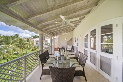 Private balcony of Sunshine View Penthouse at Sugar Hill Resort, Barbados, with outdoor dining area, wicker furniture, and ceiling fans, offering a relaxing space to enjoy views of the resort's lush gardens and Caribbean breezes.