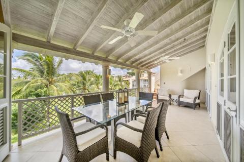Dining area on the balcony of Sunshine View Penthouse, Sugar Hill Resort, Barbados, with a glass-top table and wicker chairs, surrounded by tropical palm trees, making it an ideal spot for al fresco dining in a tranquil setting.