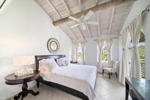 Master bedroom of Sunshine View Penthouse at Sugar Hill Resort, Barbados, with high vaulted ceilings, a plush king-size bed, and large windows that fill the space with natural light, offering a peaceful retreat overlooking the lush resort landscape.