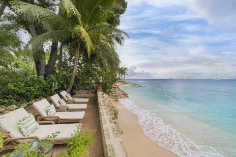 Sun loungers on the private beach at Seascape, Barbados, shaded by swaying palm trees and offering unmatched relaxation for holiday rental guests seeking luxury and tranquility.